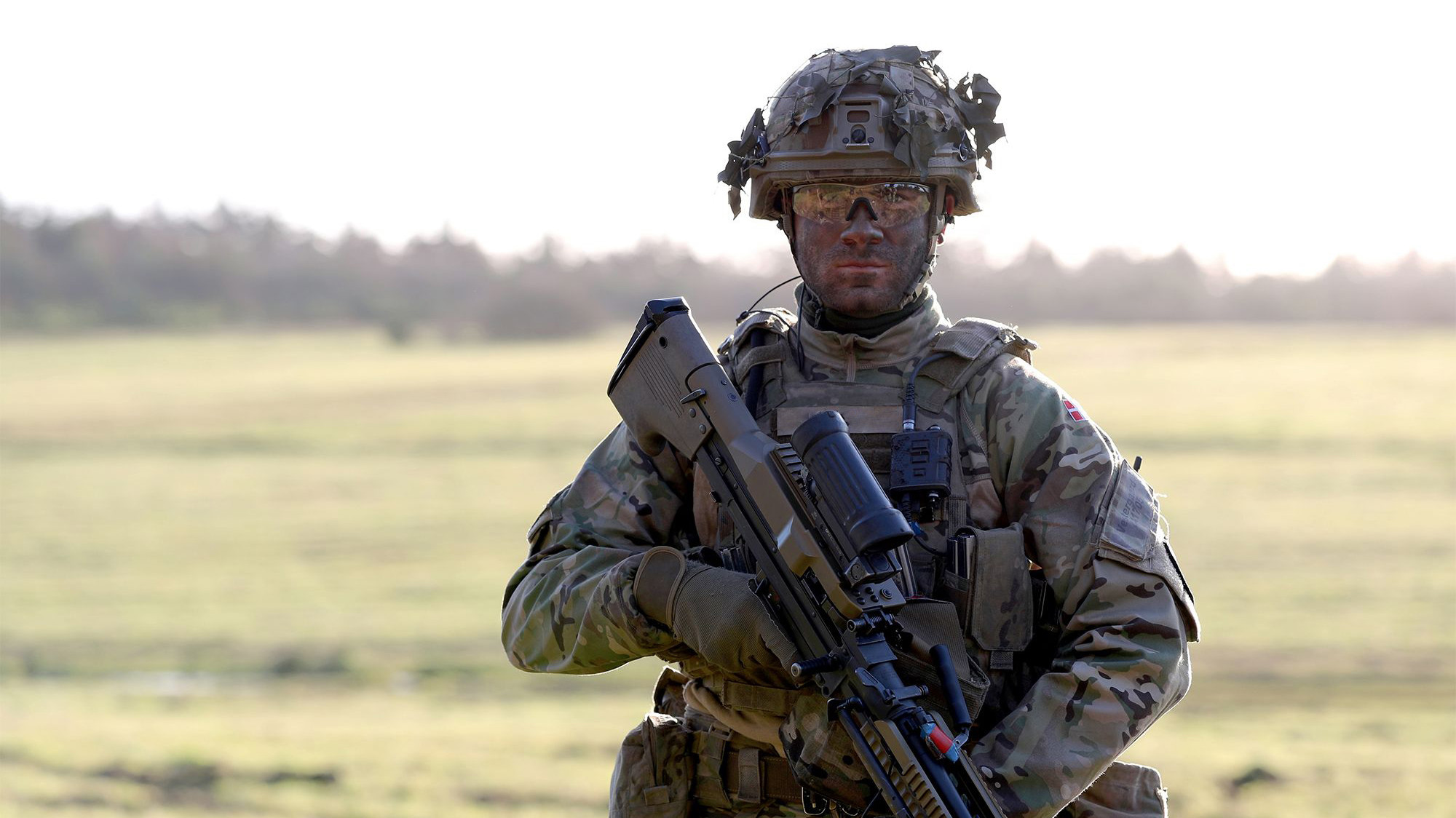 Soldat kigger ud på kameraet i uniform og fuldt udstyr