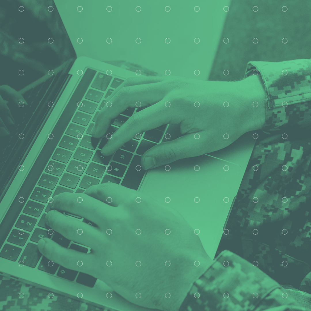 Person i militært tøj skriver på en bærbar computer med grønne farvetoner.