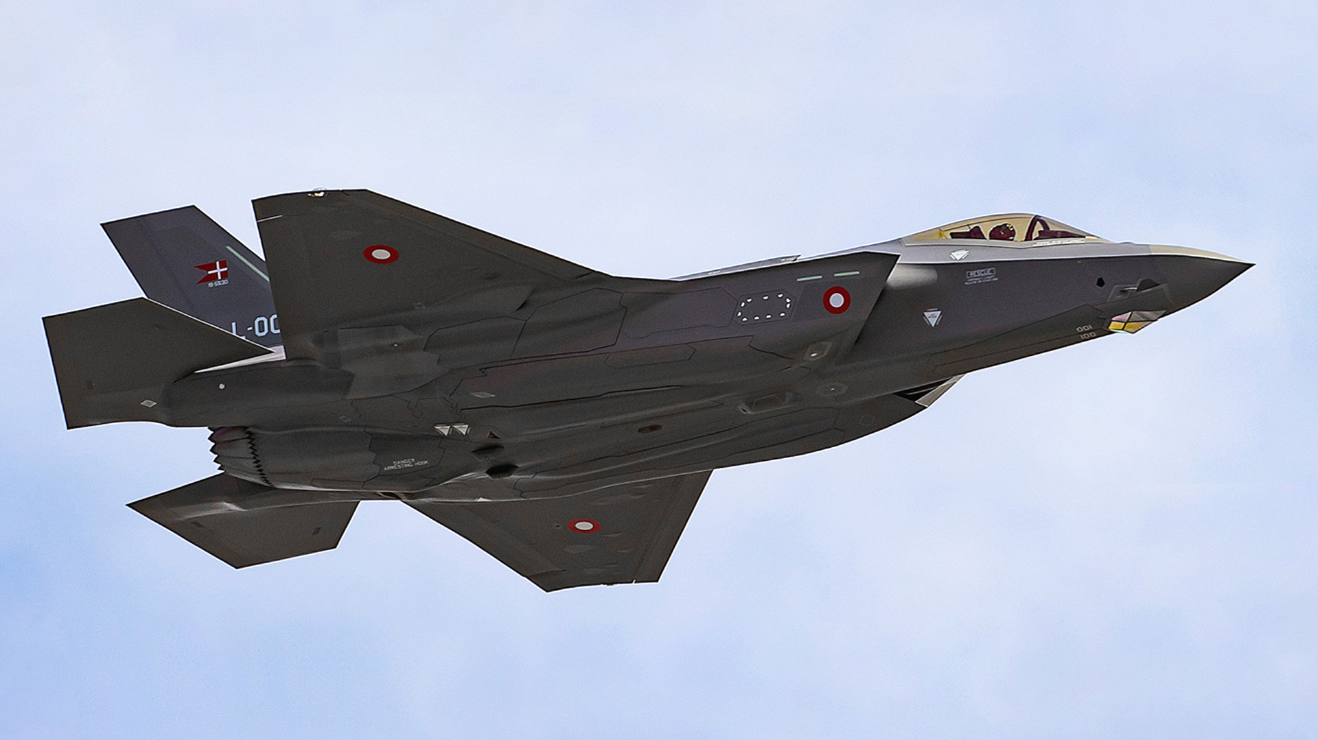 Moderne stealth-jagerfly med slankt, kantet design og militærmærker flyver under delvist skyet himmel.