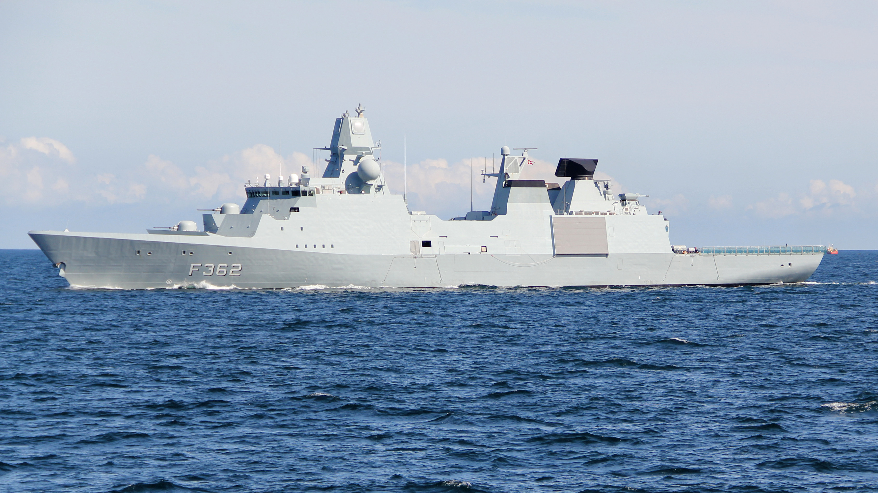 Moderne flådefartøj med gråt, strømlinet skrog og nummeret "F362" sejler på åbent hav under klar himmel.