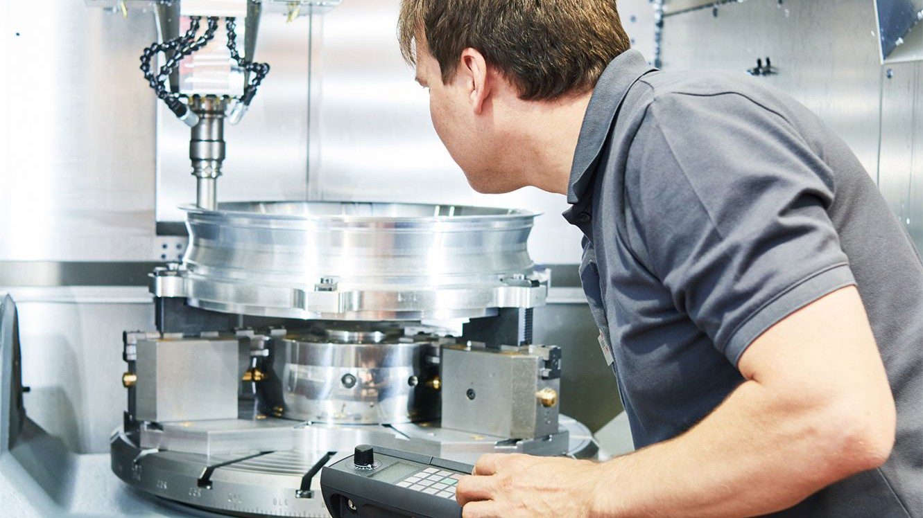 Tekniker undersøger værktøjsmaskine med avanceret styrepult i industriel, moderne omgivelser. Fokus på kvalitetssikring.