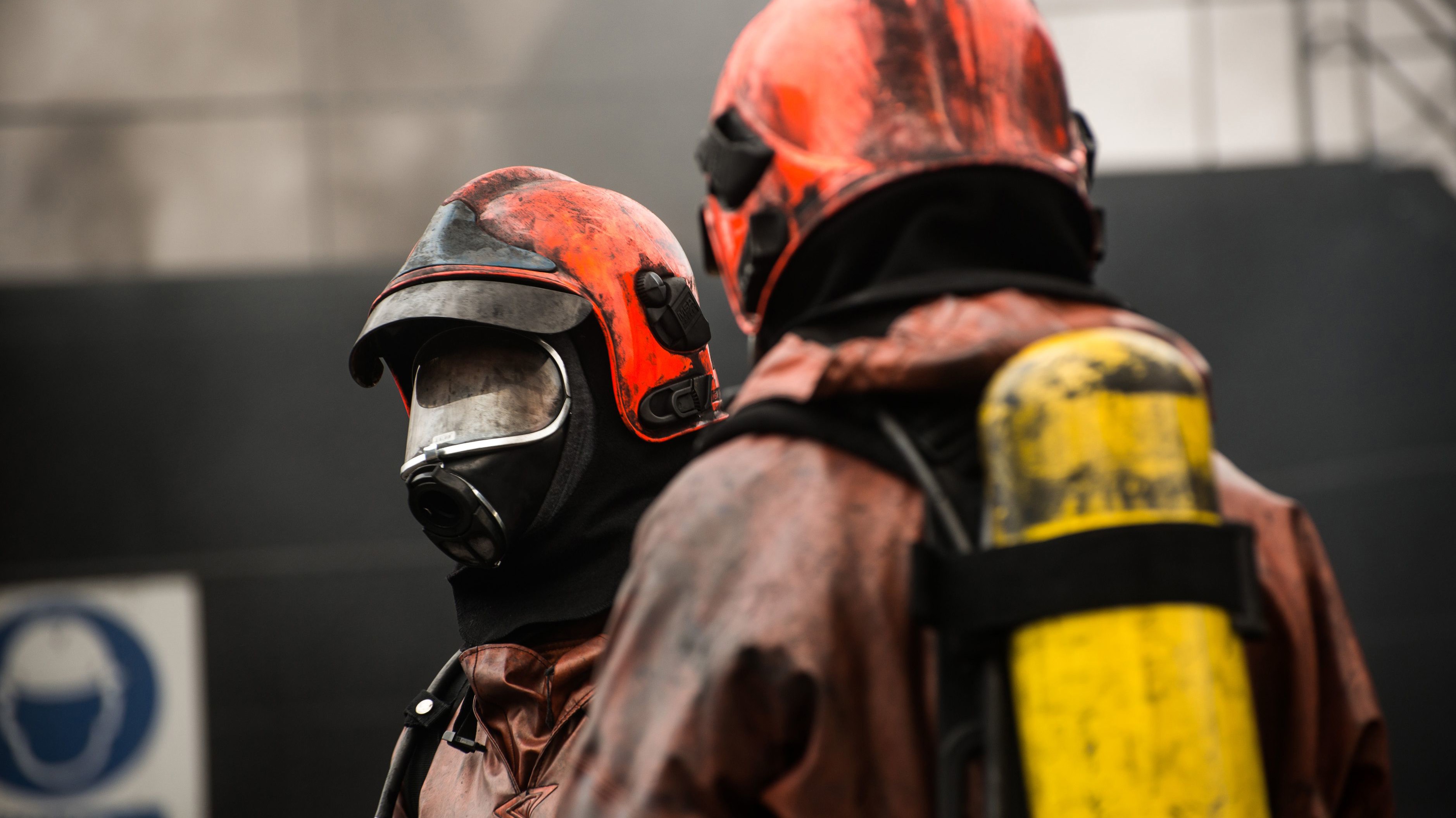 To beredskabsfolk i branddragter og hjelme arbejder i røgfyldt miljø med åndedrætsværn.