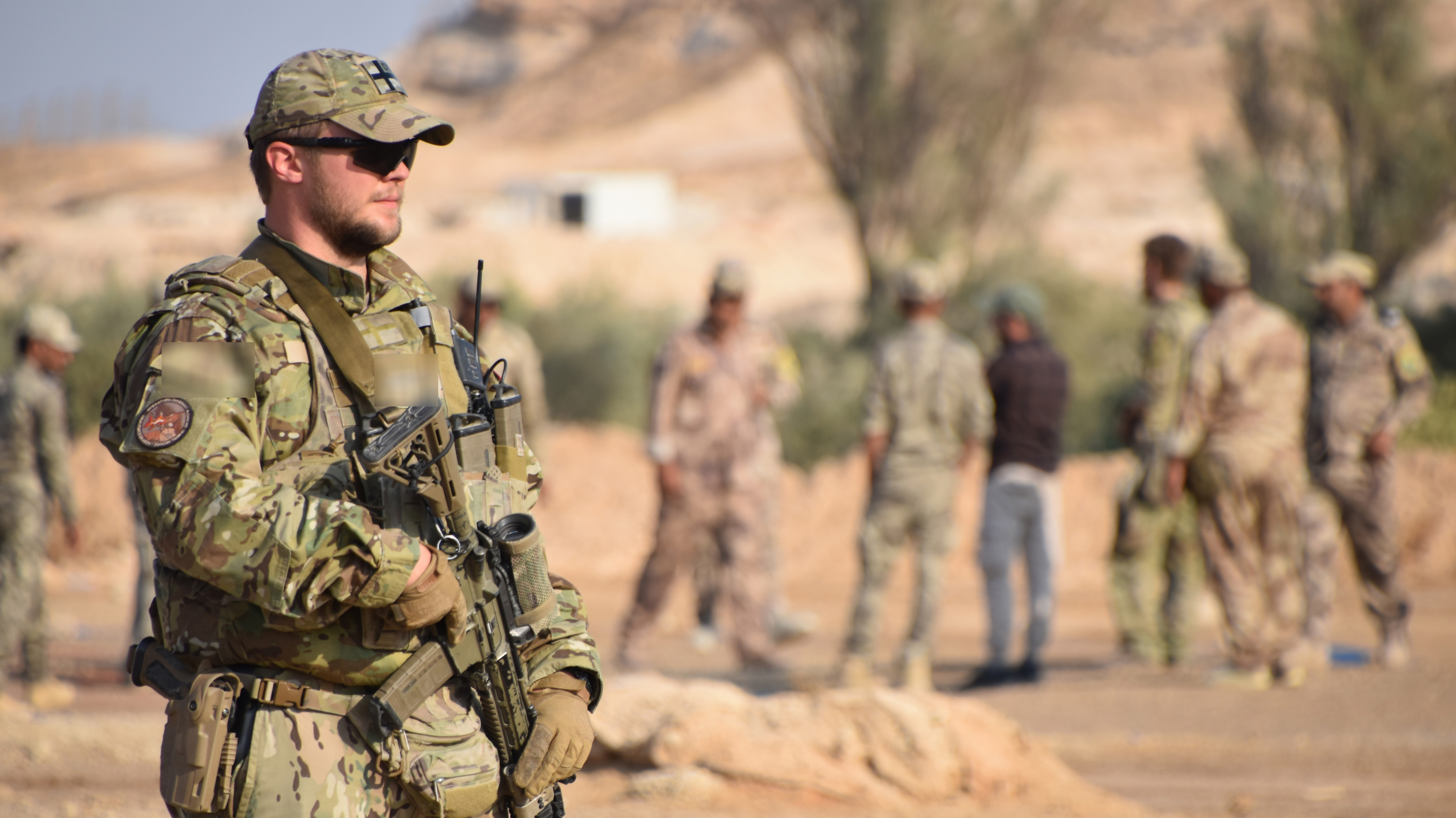 En soldat i uniform i et ørkenlandskab med folk i baggrunden.
