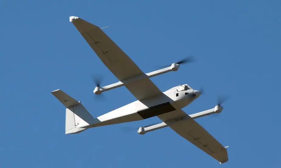 Fastvinget drone med lang vingefang og flere propeller flyver mod klar blå himmel, sandsynligvis et prototype uden mærkning.