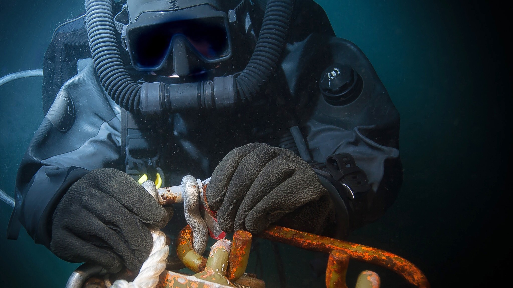 Dykker i tørdragt arbejder med rusten metalgenstand under vand.