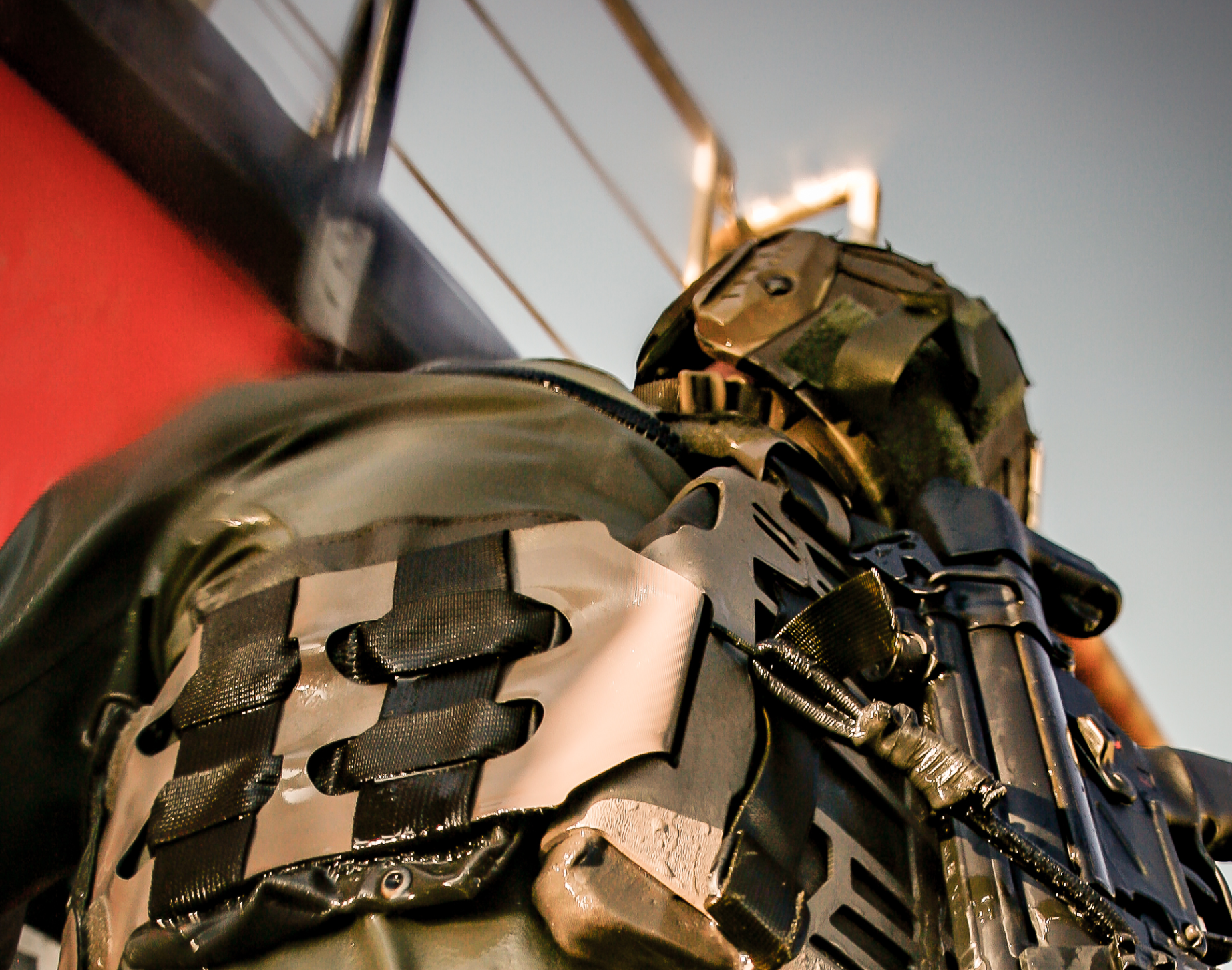 Person iført taktisk udstyr med camouflagehjelm og vest med remme og lommer i et maritimt eller industrielt miljø.