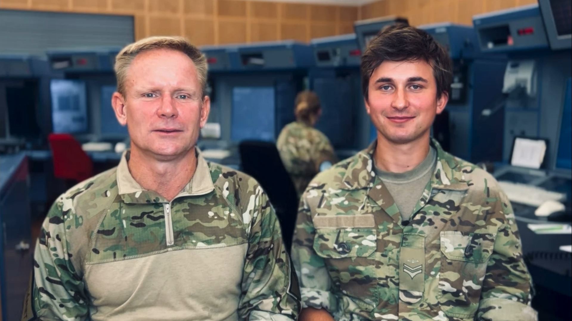 En flyveleder og identification operator står i kontrolrummet i uniform og smiler til kameraet