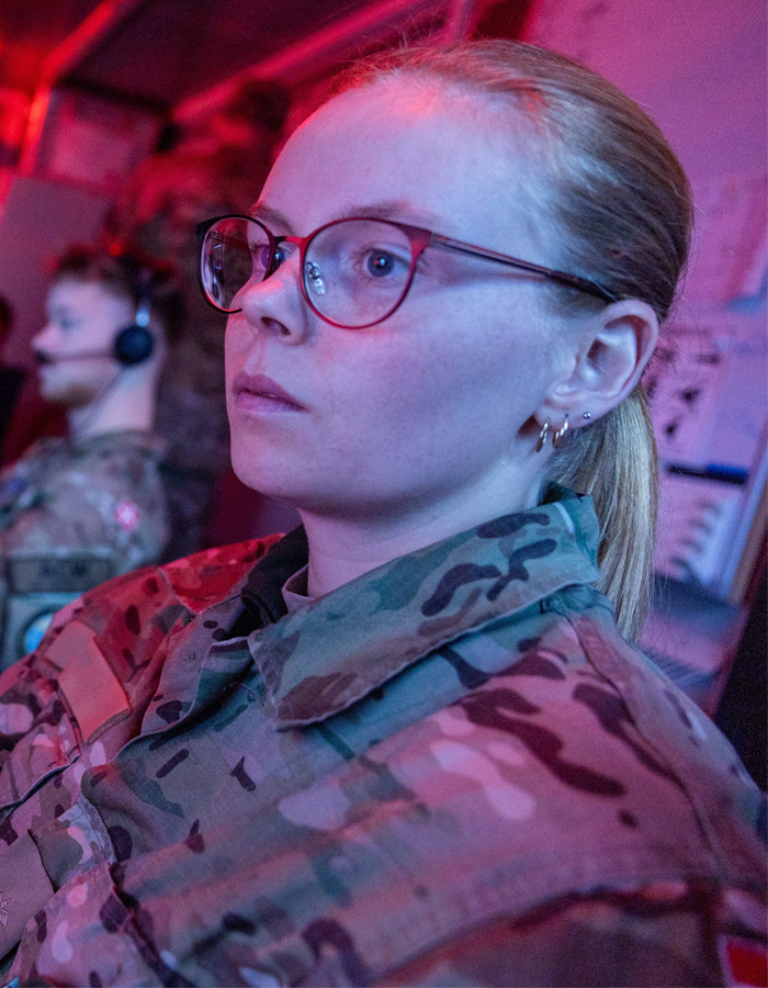 Kvindelig soldat sidder foran skærm i et rum med rødt lys