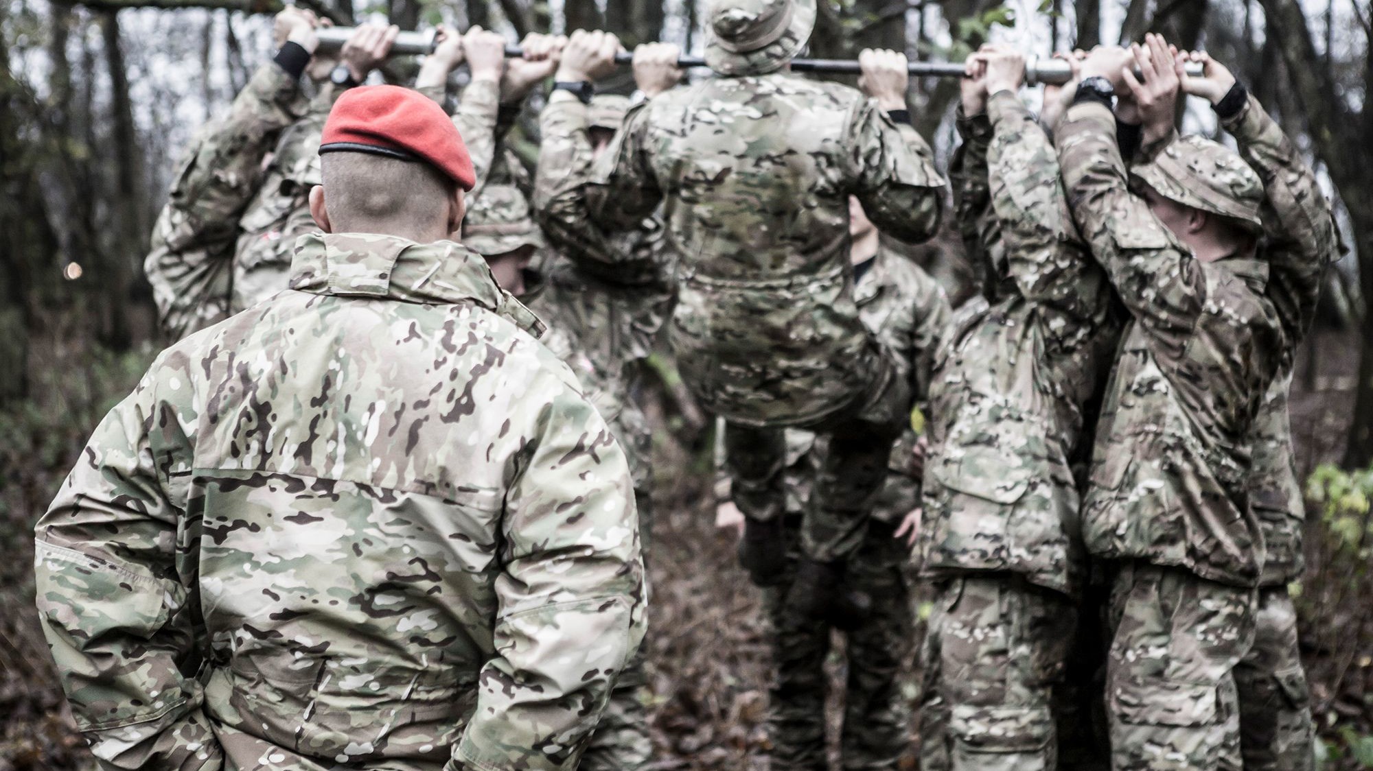 Militærpoliti i felten med synligt MP-mærke og mærke med to krydsede pistoler og krone. Tre soldater i baggrunden står med slørede ansigter og våben.