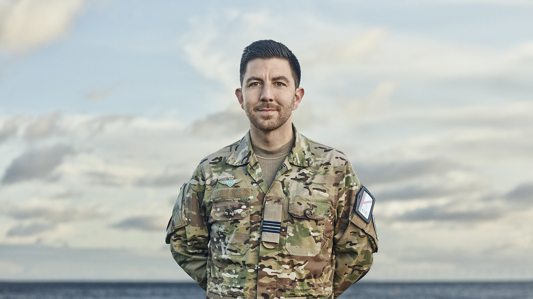 En officer i flyvevåbnet kigger ud på kameraet med armene bag ryggen og smiler.