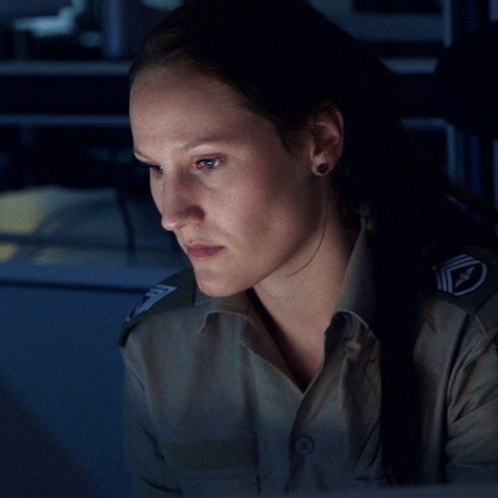 Kvindeligt sergent sidder med front mod skærm i mørkt rum