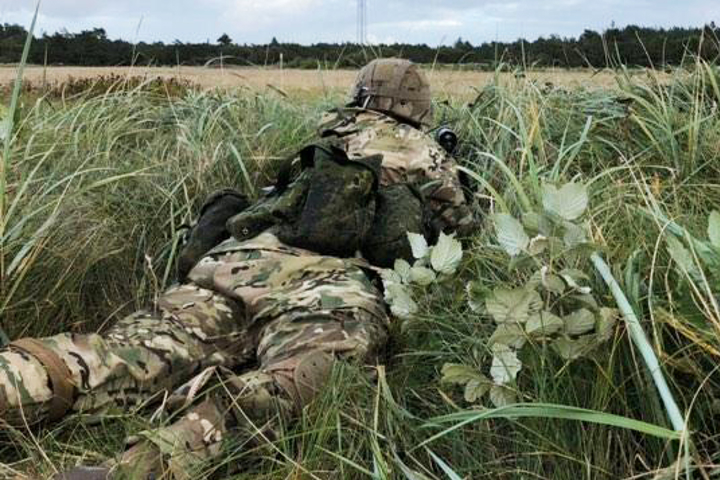 Kristina ligger i uniform i græsset og spejder ud over marken