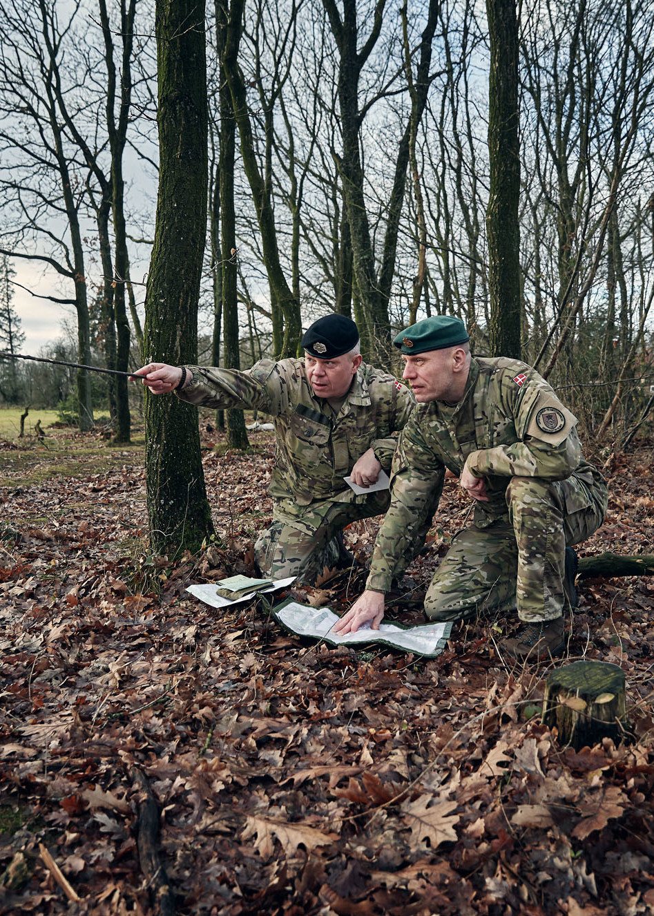 To uniformklædte mænd sidder i skovbunden og kigger på kort. Dene ene peger mod den retning de skal.