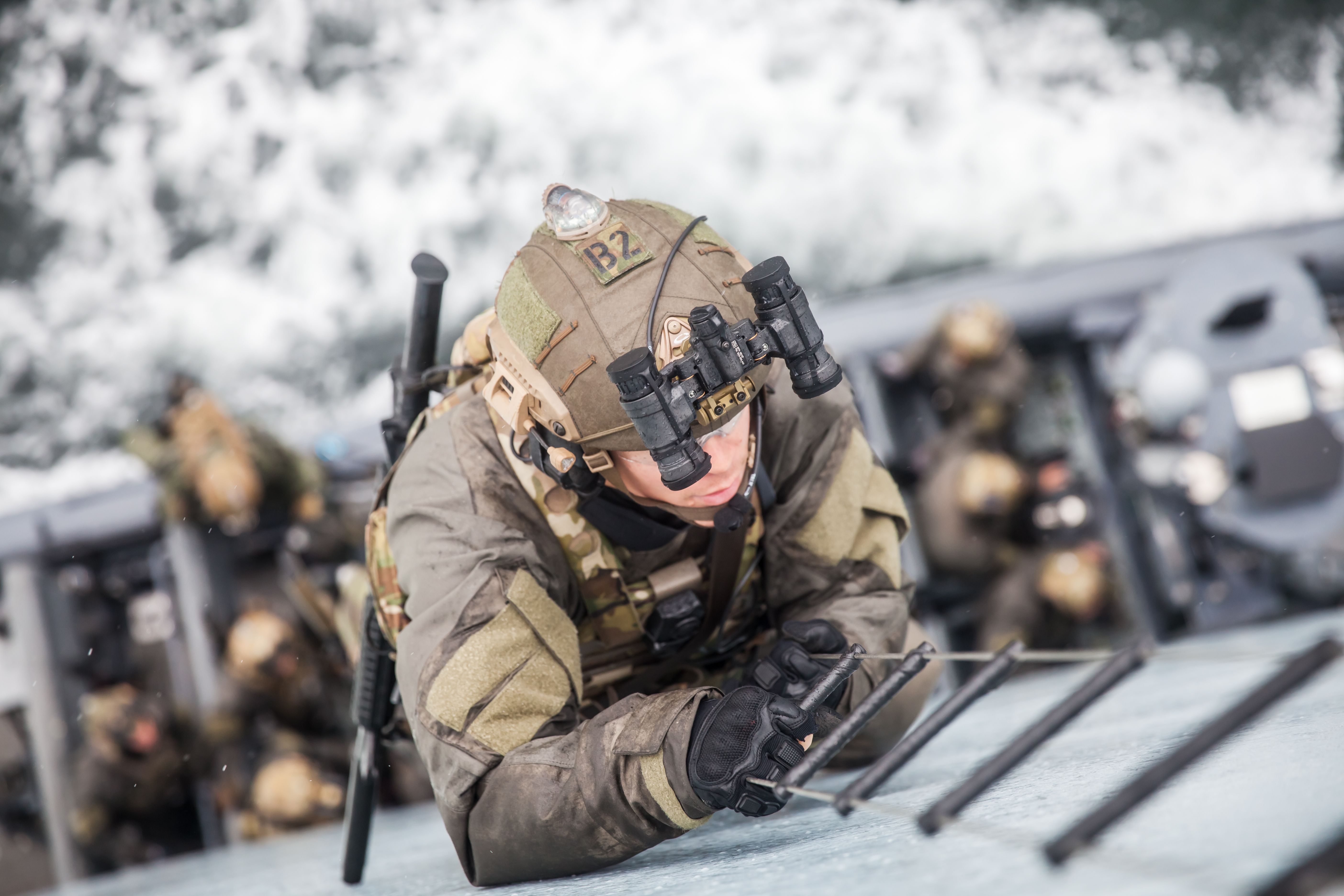 Soldat med natoptik og taktisk udstyr klatrer op ad en rebstige fra en båd under en maritim operation.