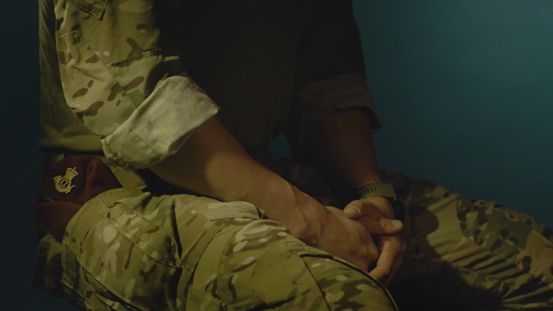 erson i camouflageuniform med bordeaux baret og foldede hænder i skødet.