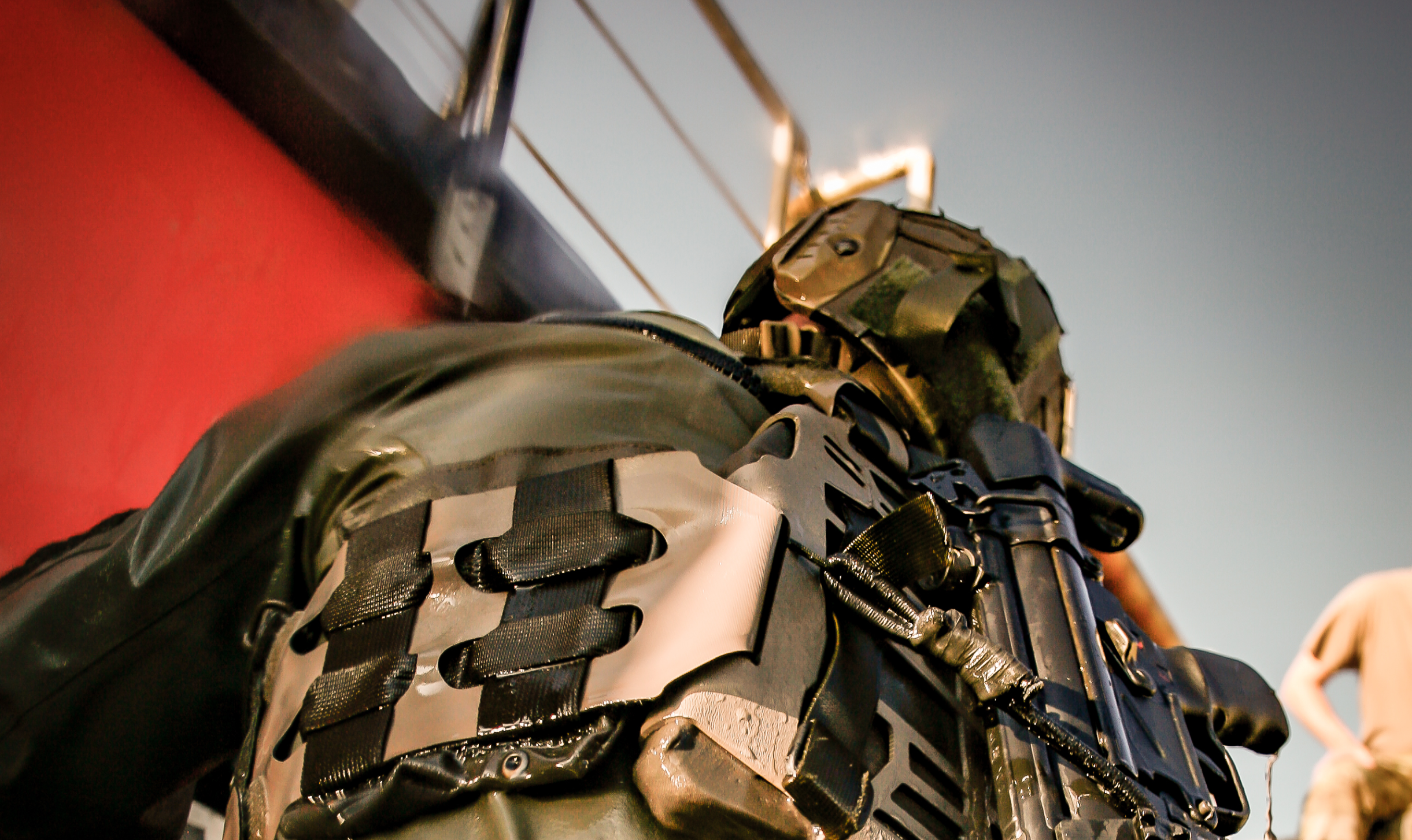 Nærbillede bagfra af en soldat i våddragt og kampudstyr, i færd med at borde et fartøj via en stige.