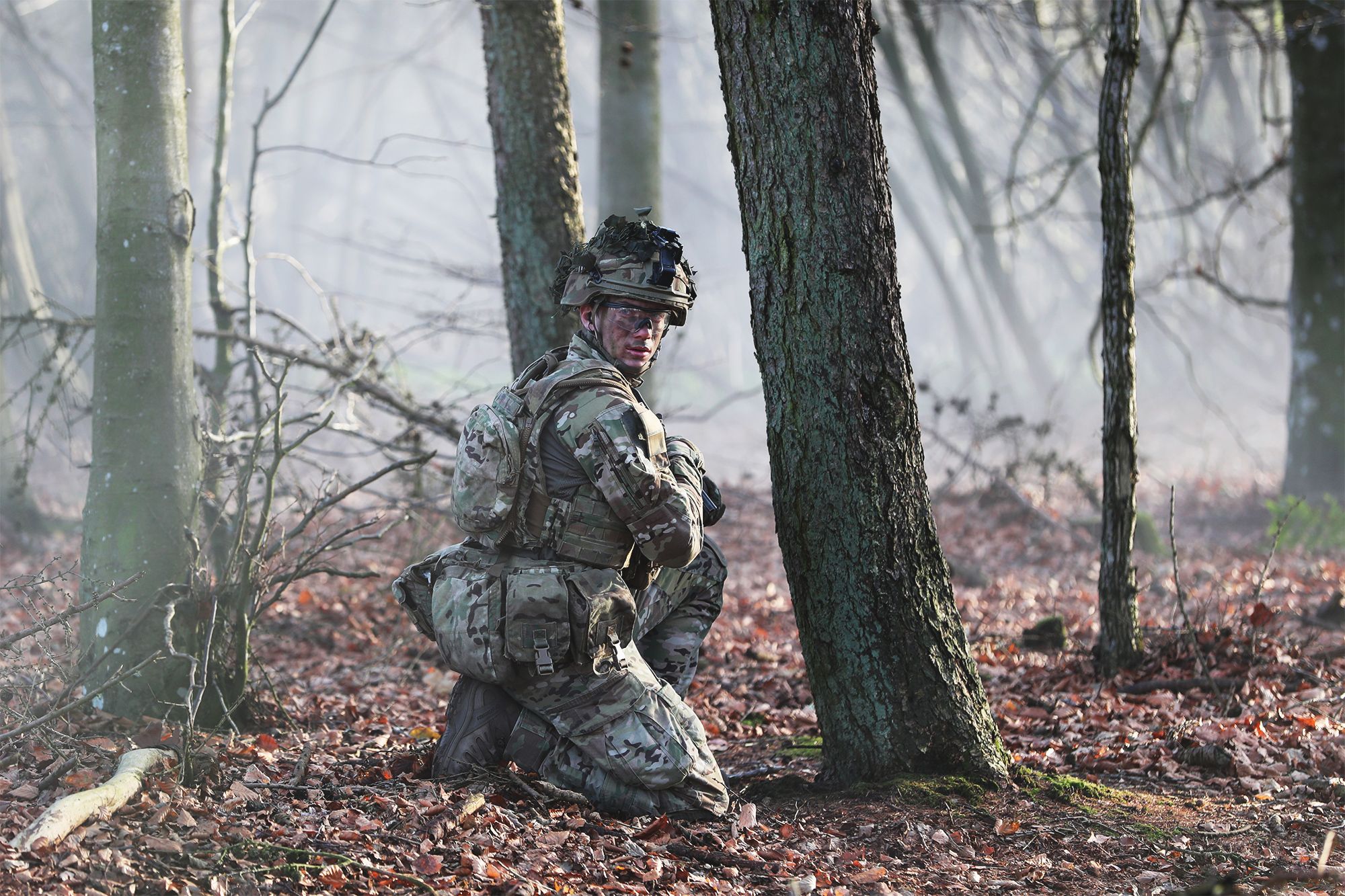 Soldat sidder på hug i skoven og kigger mod kameraet