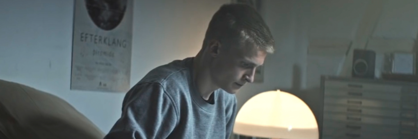 En ung person sidder på en seng i et dæmpet oplyst værelse og arbejder på en bærbar computer.