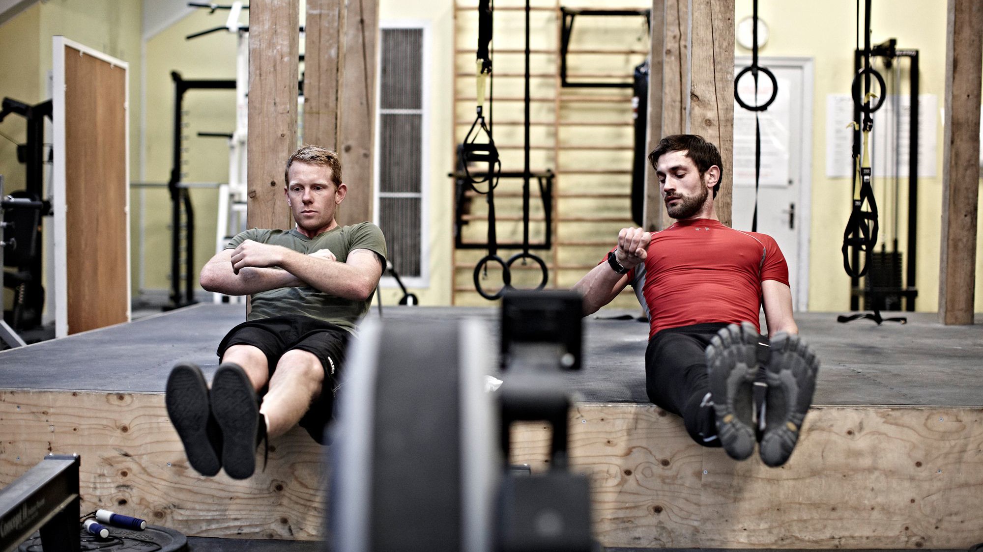 To mænd laver core-træning side om side i et træningslokale.