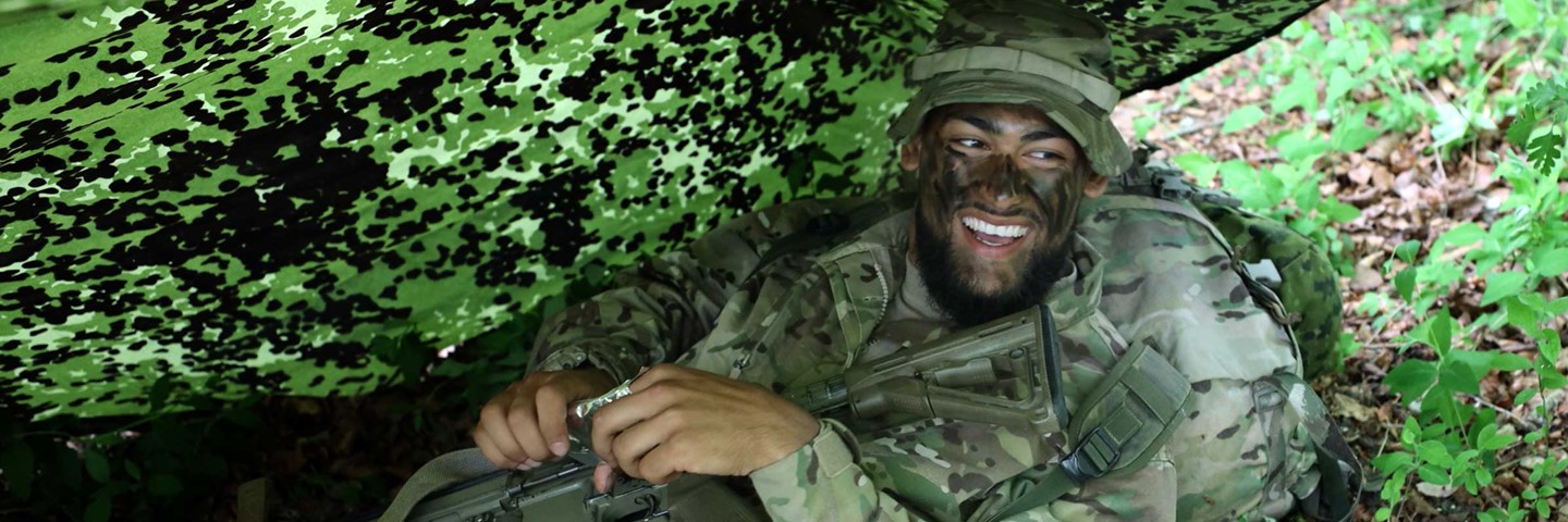 Soldater ligge under camouflage teltdug