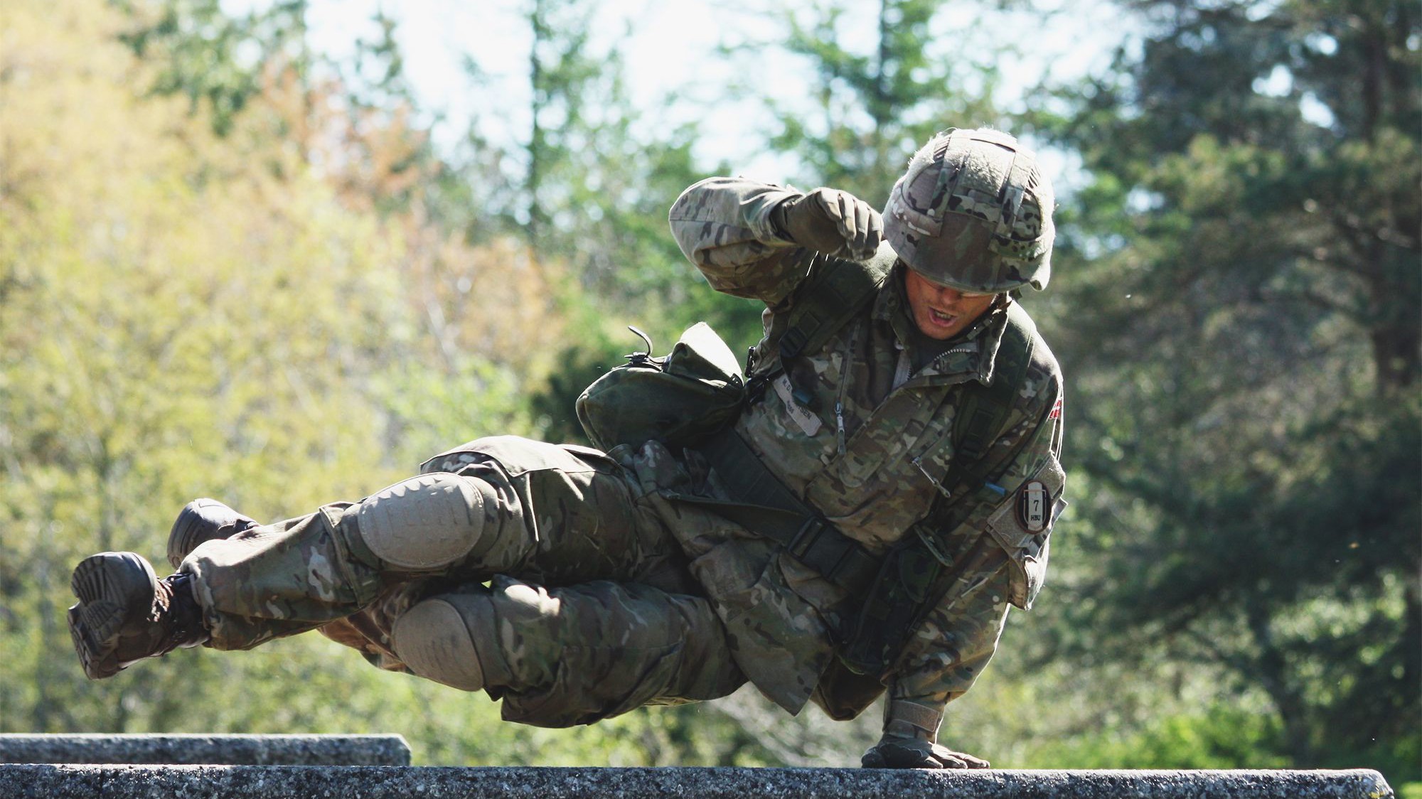 Værnepligtig soldat i fuld uniform gennemfører en forhindring på en udendørs bane.