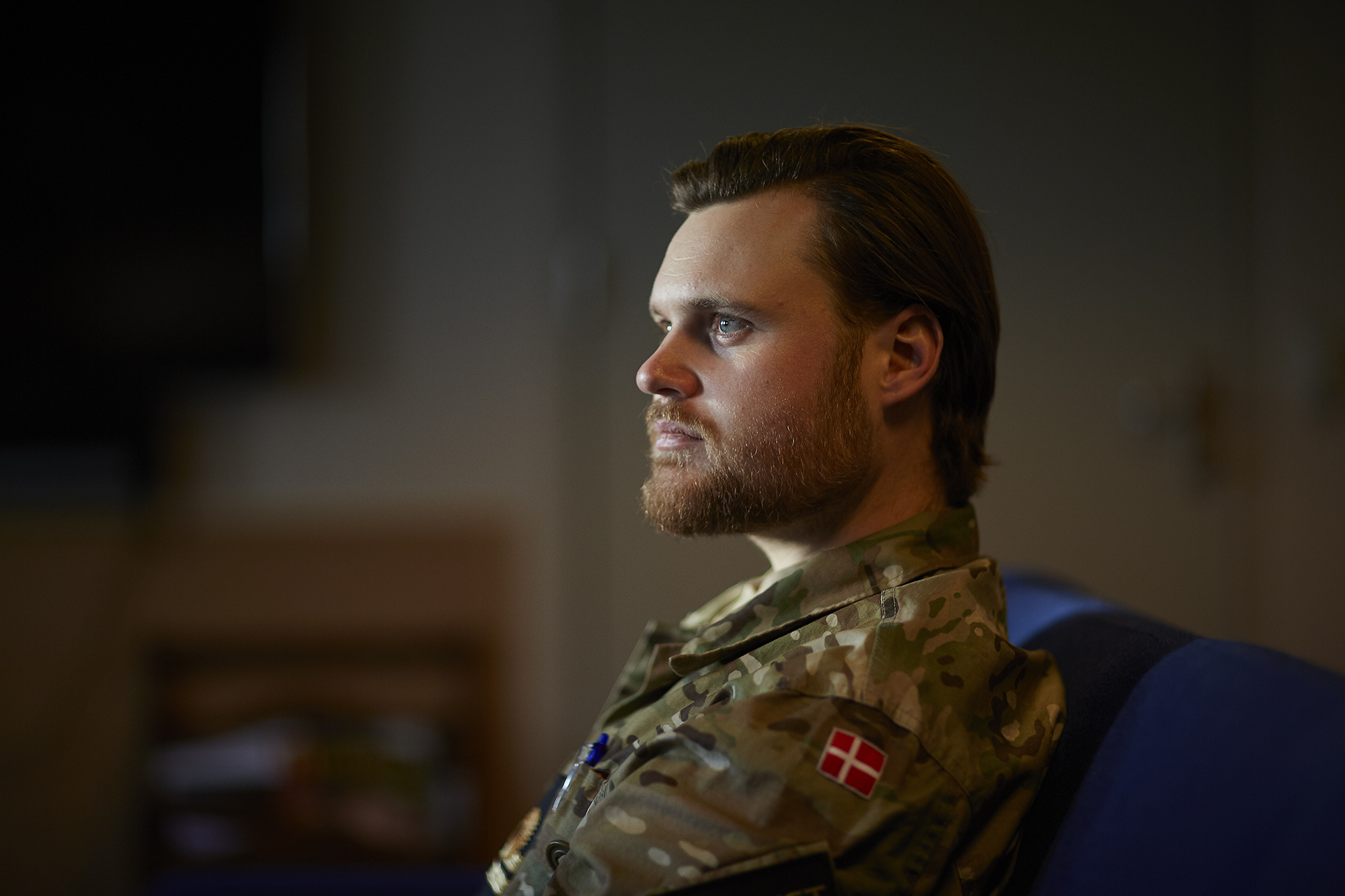 Dansk soldat i profil med velplejet skæg og langt hår, iført uniform med dansk mærke, sidder i eftertænksom stemning.